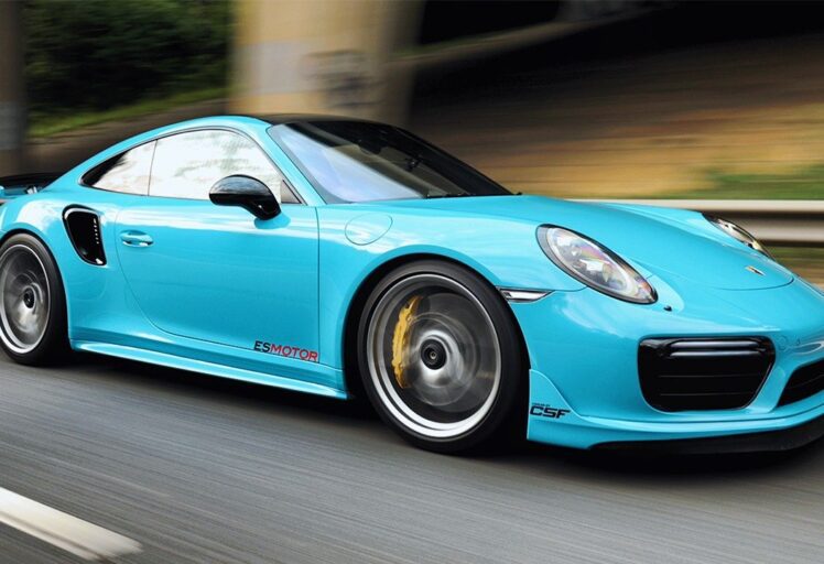 Blue Porsche sports car with "ESMOTOR" and "CSF" logos driving on a highway.