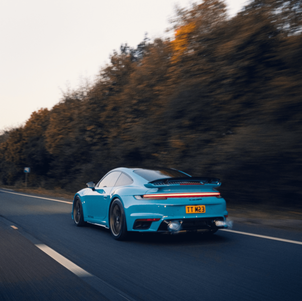 Blue Porsche driving on a highway with trees in the background.