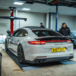 A white Porsche Turbo in a garage with two mechanics nearby.