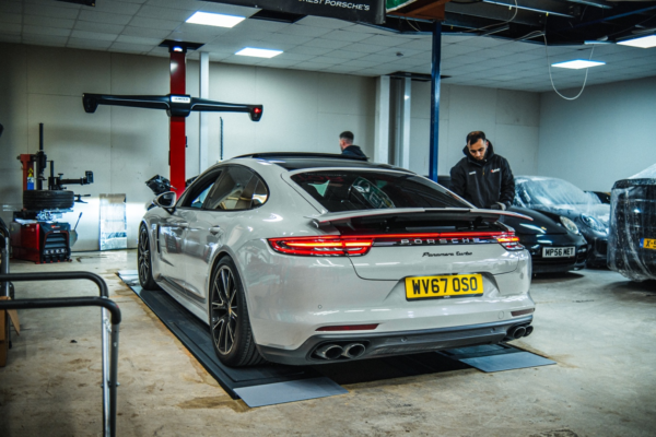 A white Porsche Turbo in a garage with two mechanics nearby.