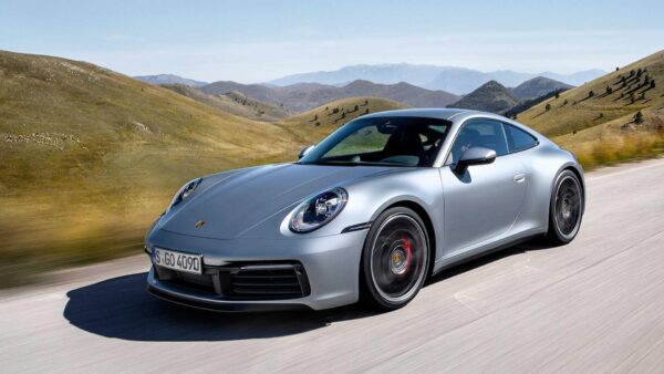 Silver Porsche 911 driving on a scenic road with hills.